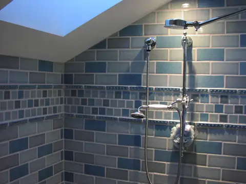A tiled walk-in shower with a dual shower head and a tile accent band